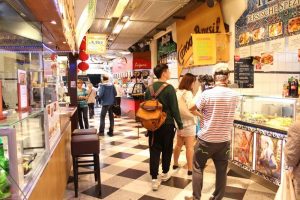 Ein Gang in der Markhalle Freiburg. Links und rechts von ihm reihen sich die Essensstände aneinander