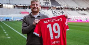Der bärtige Niklas Beste hält auf dem Rasen des leeren Europa-Park-Stadions das rote Trikot mit der Nummer 19 in die Kamera, das er künftig beim SC Freiburg tragen wird.